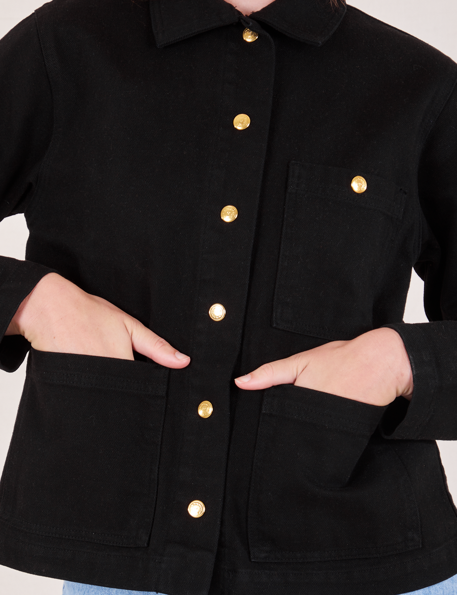 Front close up of Denim Work Jacket in Basic Black with Alex's hands in the pockets