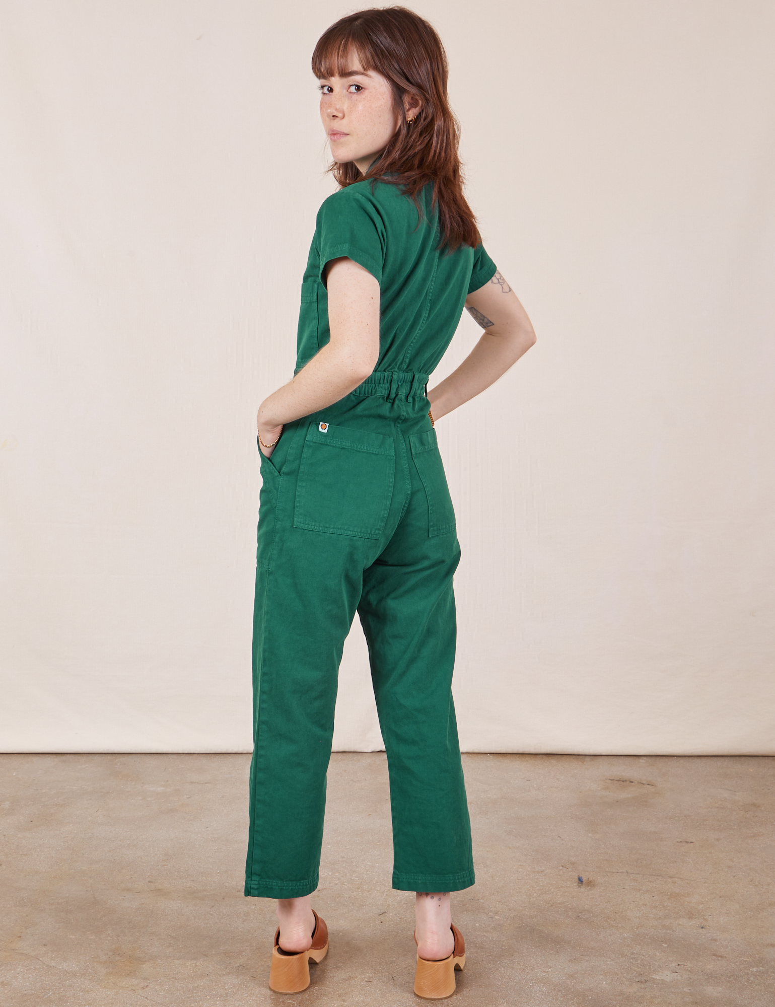 Angled back view of Petite Short Sleeve Jumpsuit in Hunter Green worn by Hana