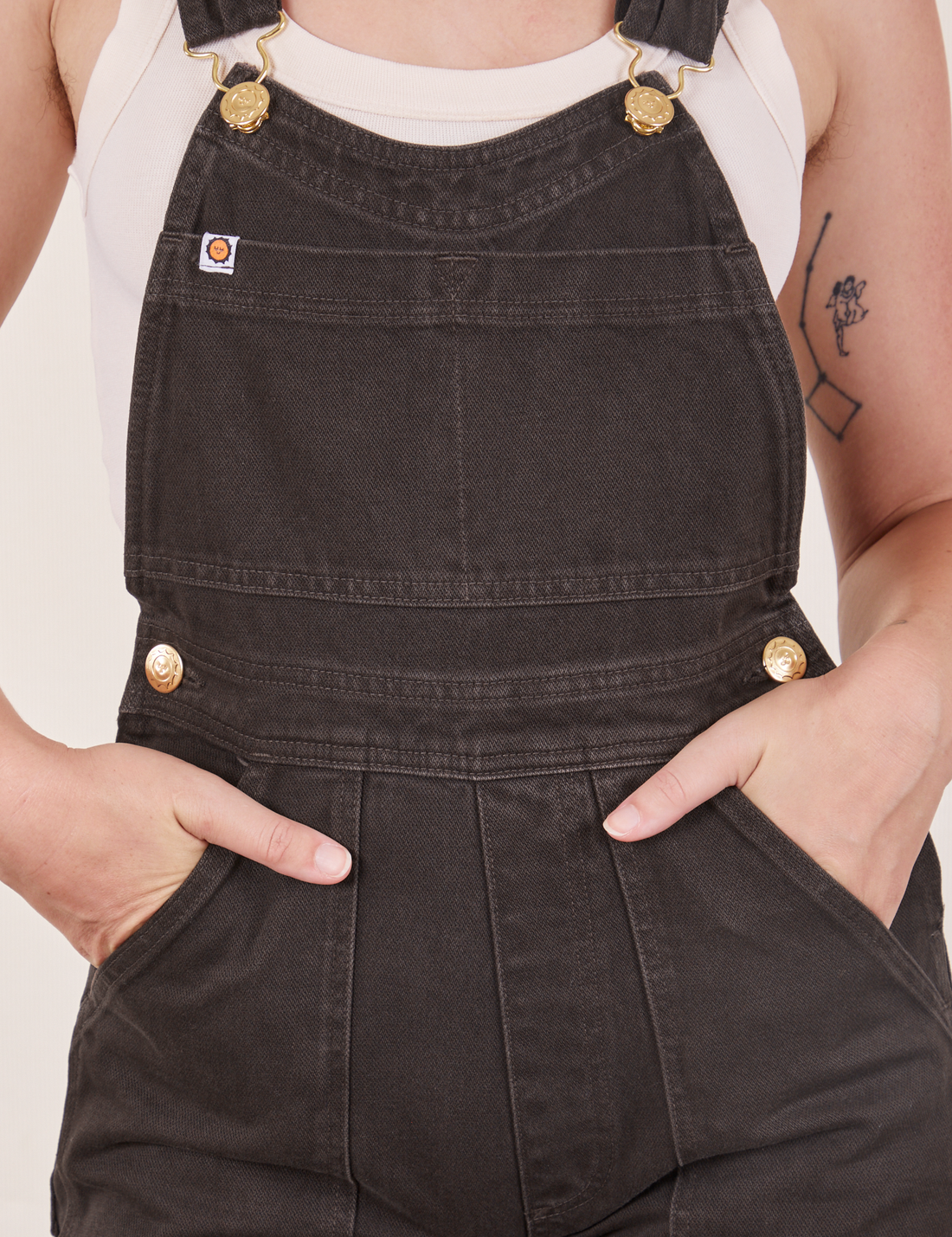 Front close up of Original Overalls in Mono Espresso. Alex has both hands in the front pockets.
