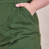 Front pocket close up of Petite Short Sleeve Jumpsuit in Dark Emerald Green. Ashley has her hand in the pocket.