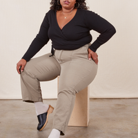 Morgan is sitting on a wooden crate wearing Work Pants in Khaki Grey and a black Wrap Top