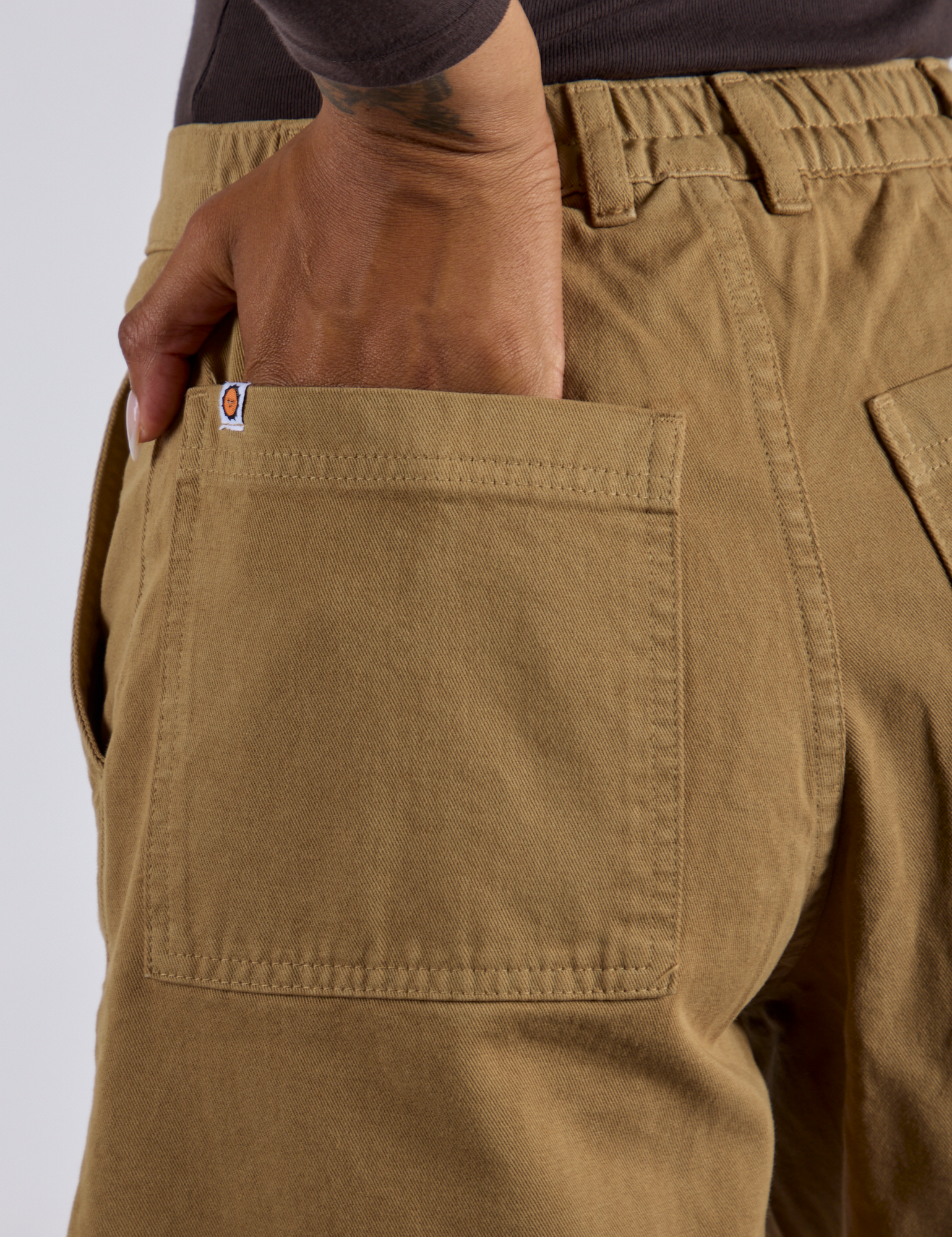 Close up of Kira's hand in the back pocket of Longline Work Shorts in Desert Brown