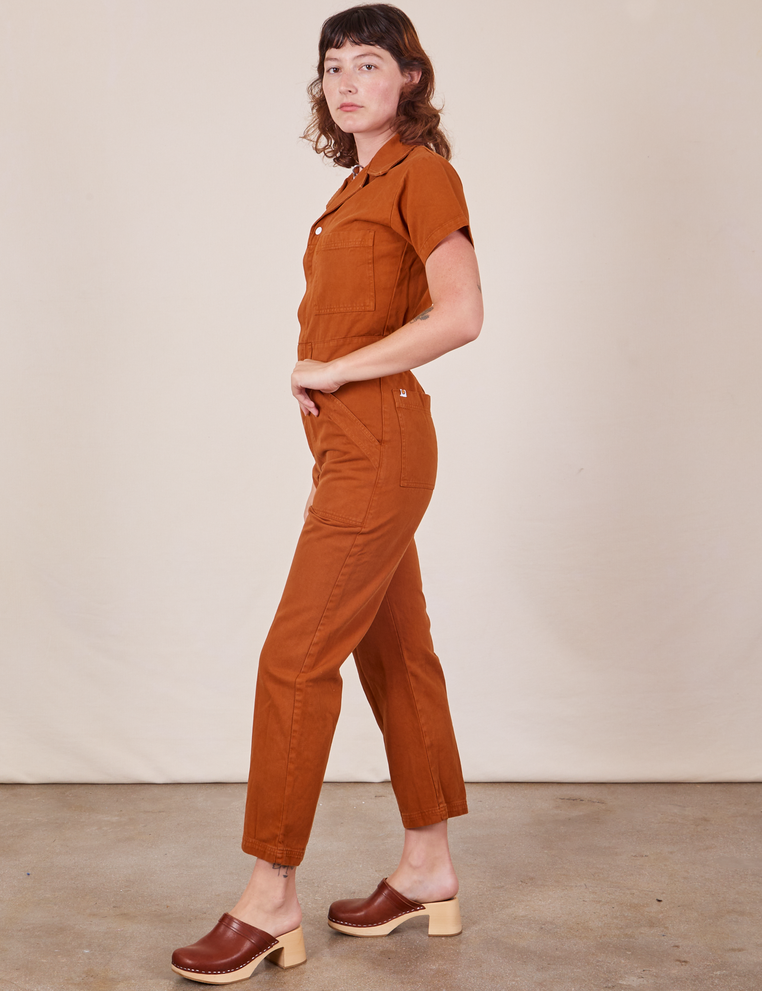 Side view of Short Sleeve Jumpsuit in Burnt Terracotta worn by Alex
