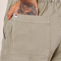 Back pocket close up of Short Sleeve Jumpsuit in Khaki Grey. Jesse has their hand in the pocket.