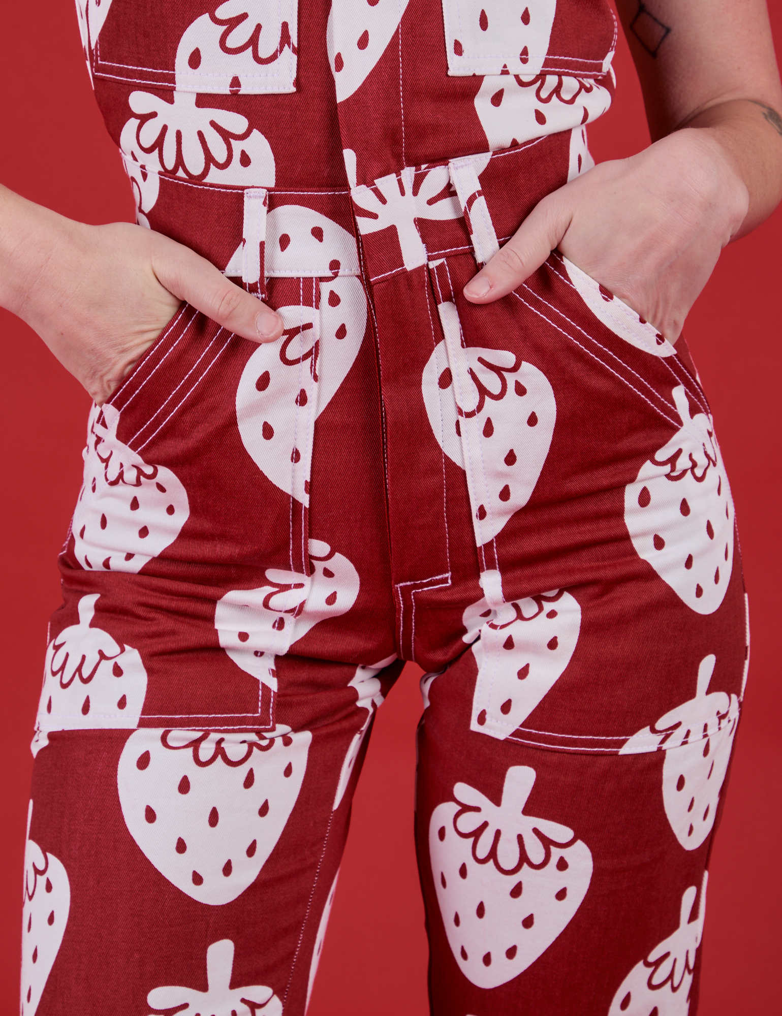 Close up of Alex's hands in the front pockets of Strawbaby Jumpsuit