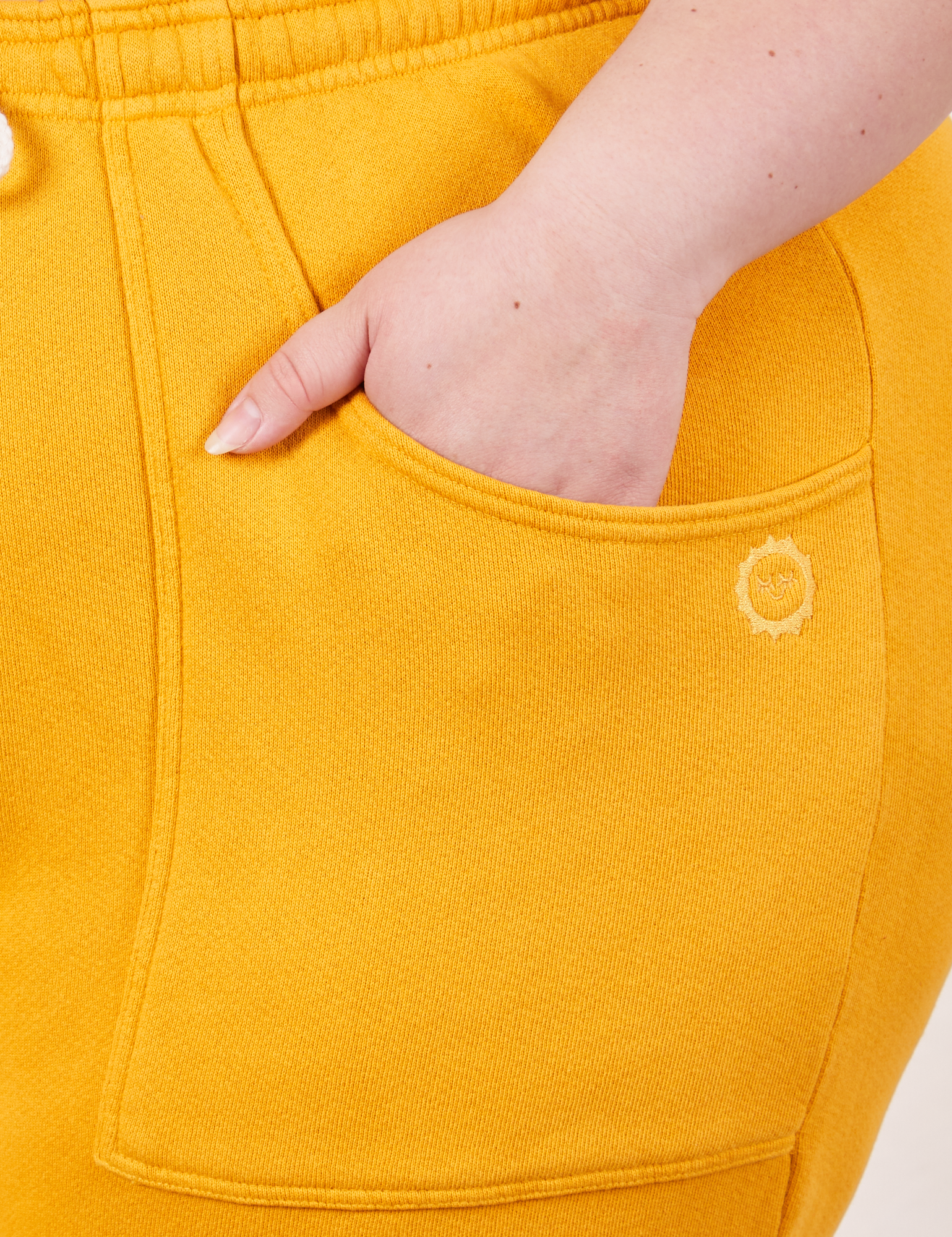 Cropped Rolled Cuff Sweatpants in Mustard Yellow front pocket close up. Ashley has her hand in the pocket.