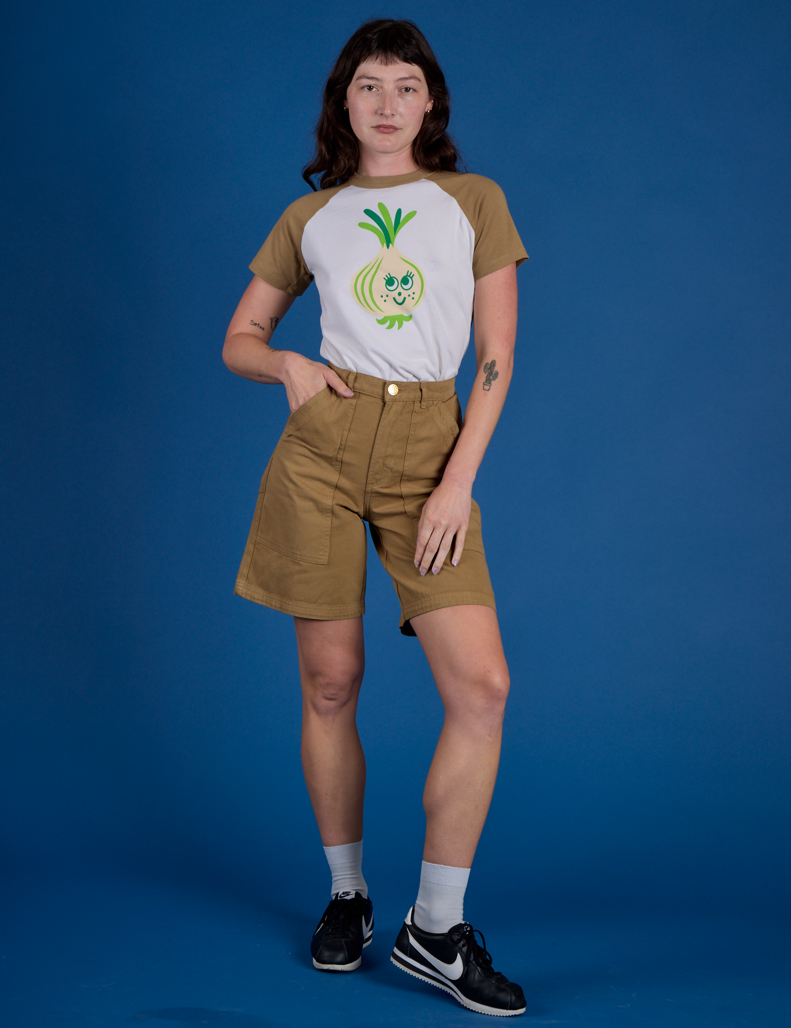 Alex is wearing Produce Raglan Tee in Onion tucked into shorts