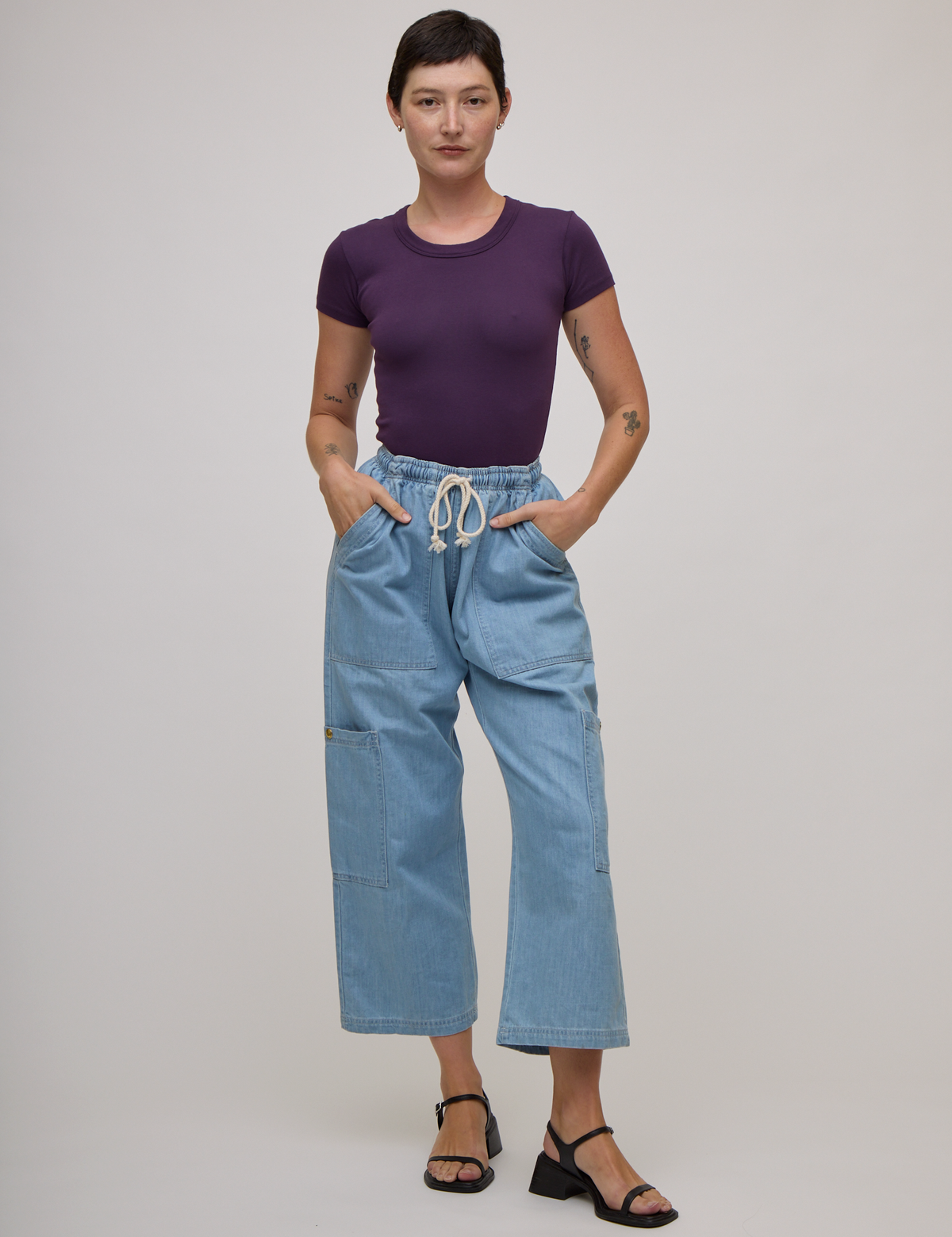 Alex is wearing Baby Tee in Nebula Purple tucked into light wash denim drop pocket pants