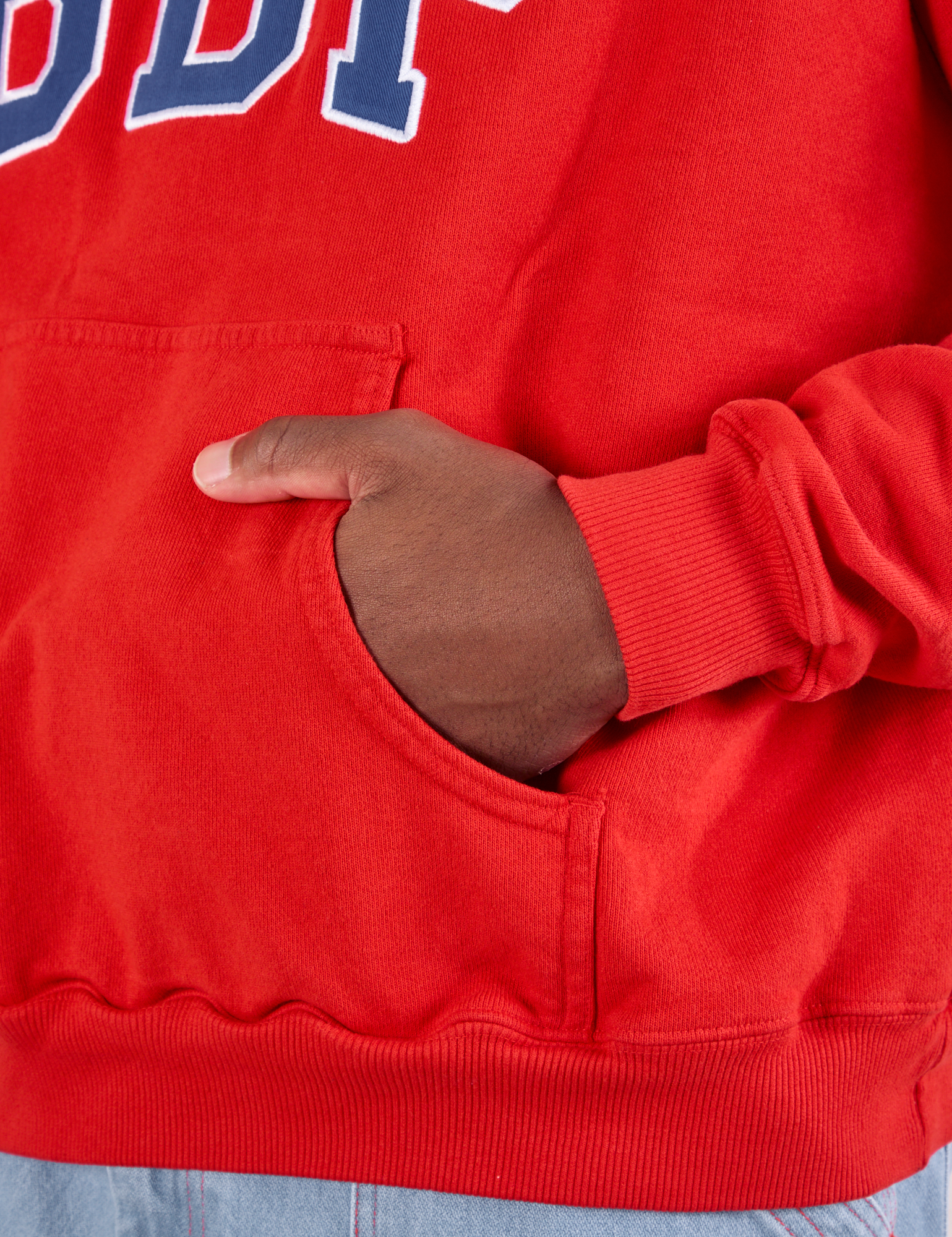 Collegiate Hoodie in Mustang Red kangaroo pocket close up. Issac has his hand in the pocket.