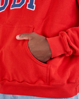 Collegiate Hoodie in Mustang Red kangaroo pocket close up. Issac has his hand in the pocket.