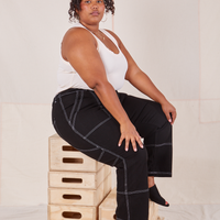 Morgan is sitting on a stack of wooden crates. She is wearing Carpenter Jeans in Black and vintage off-white Tank Top.