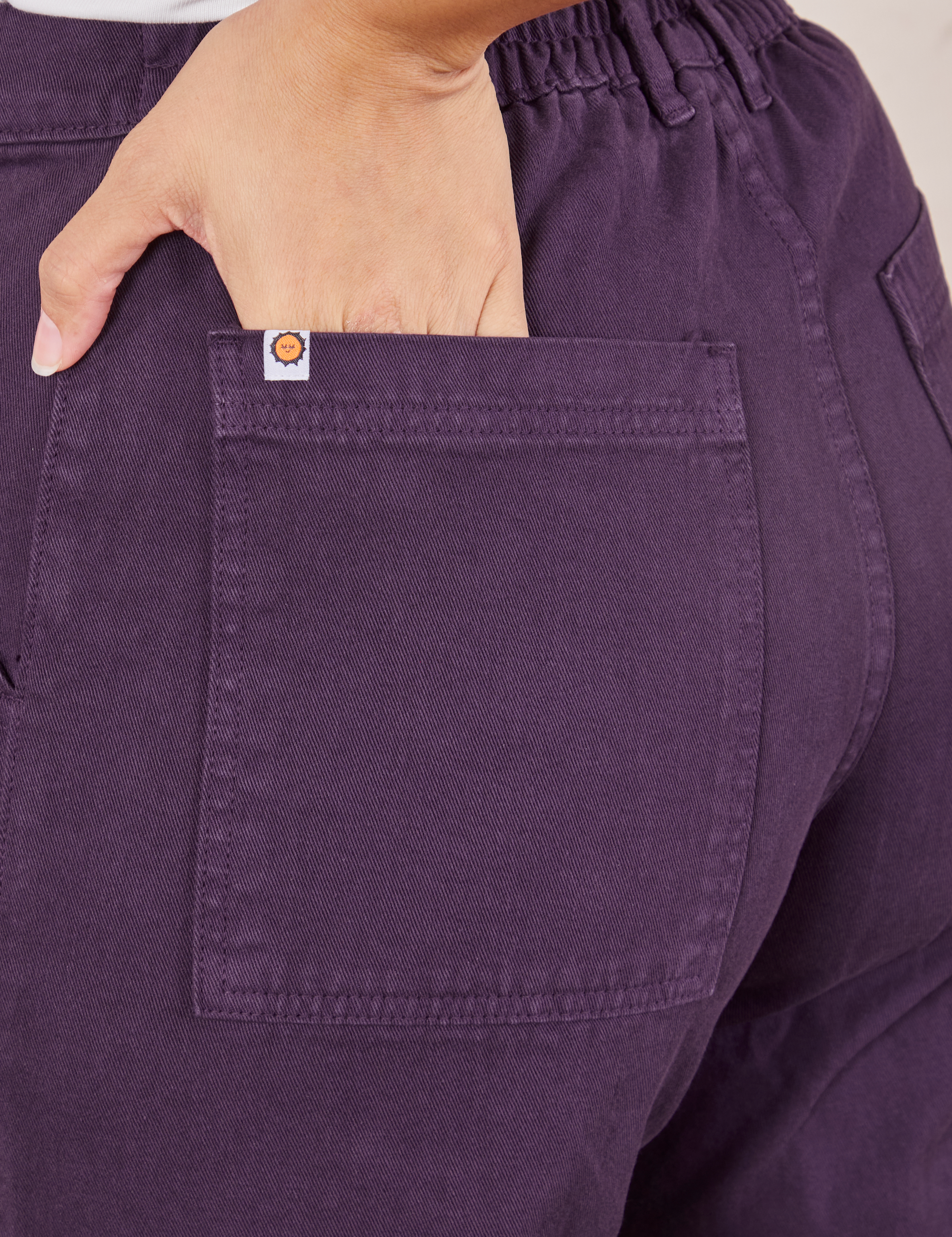 Back pocket close up of Work Pants in Nebula Purple. Tiara has her hand in the pocket.