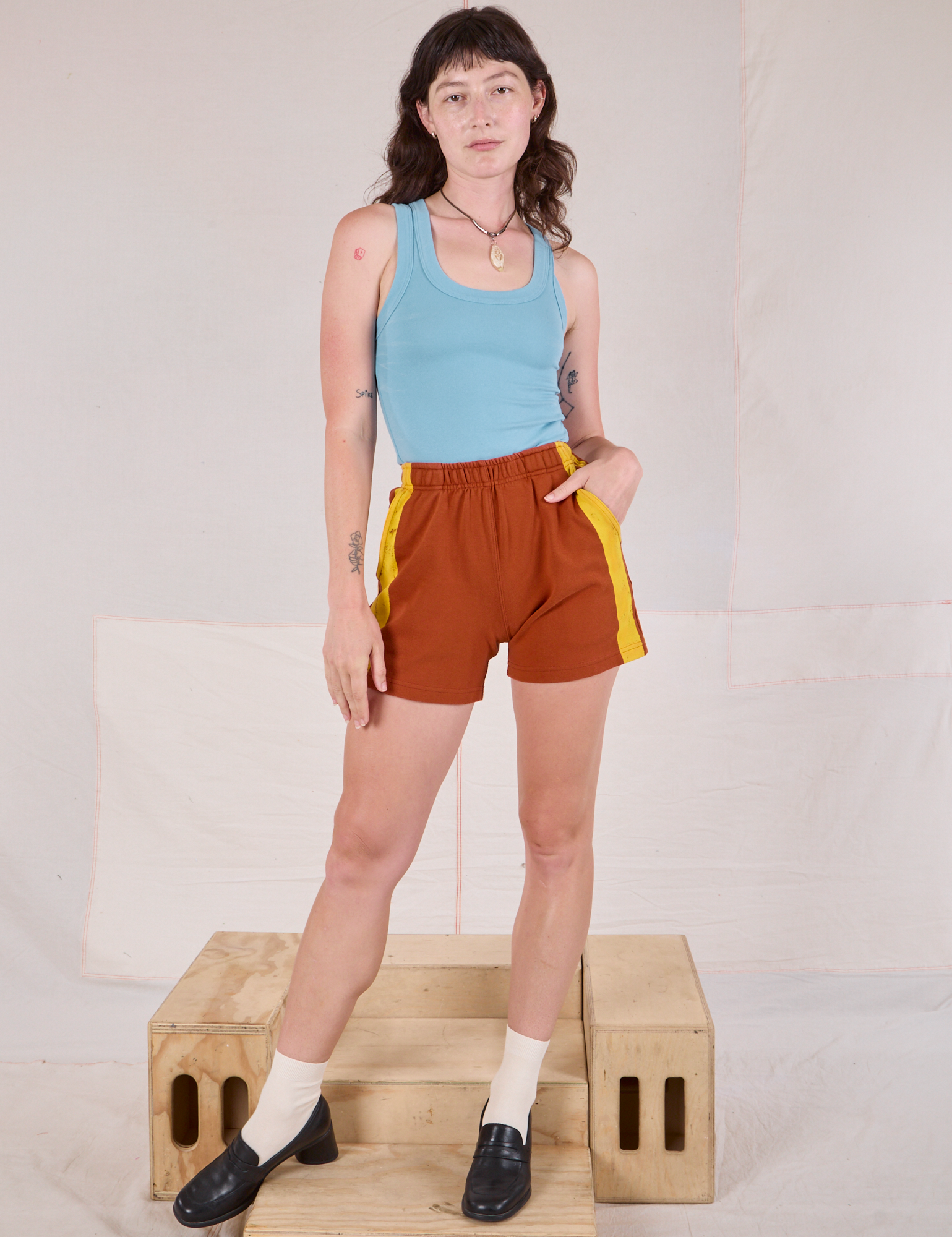 Alex is 5&#39;8&quot; and wearing P Painted Stripe Easy Shorts in Burnt Terracotta paired with a baby blue Tank Top