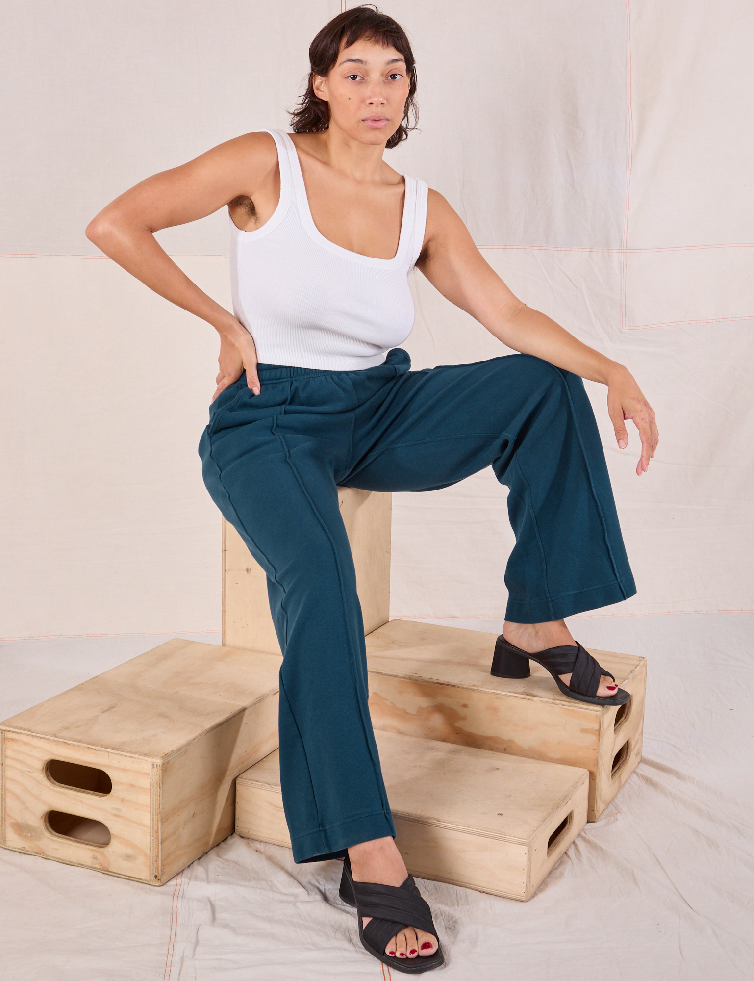 Tiara is wearing Easy Western Pants in Lagoon and sitting on a wooden crate