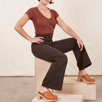 Soraya sitting on a wooden crate wearing Western Pants in Espresso Brown paired with fudgesicle brown V-Neck Tee
