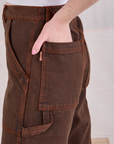 Close up of Hana's hand in the back pocket of Overdyed Carpenter Jeans in Fudge