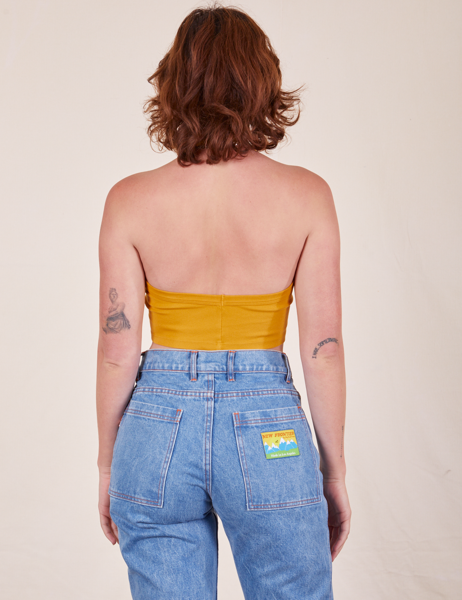 Back view of Halter Top in Mustard Yellow and light wash Frontier Jeans worn by Alex