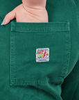 Back pocket close up of Original Overalls in Mono Hunter Green. Ashley has her hand in the pocket.