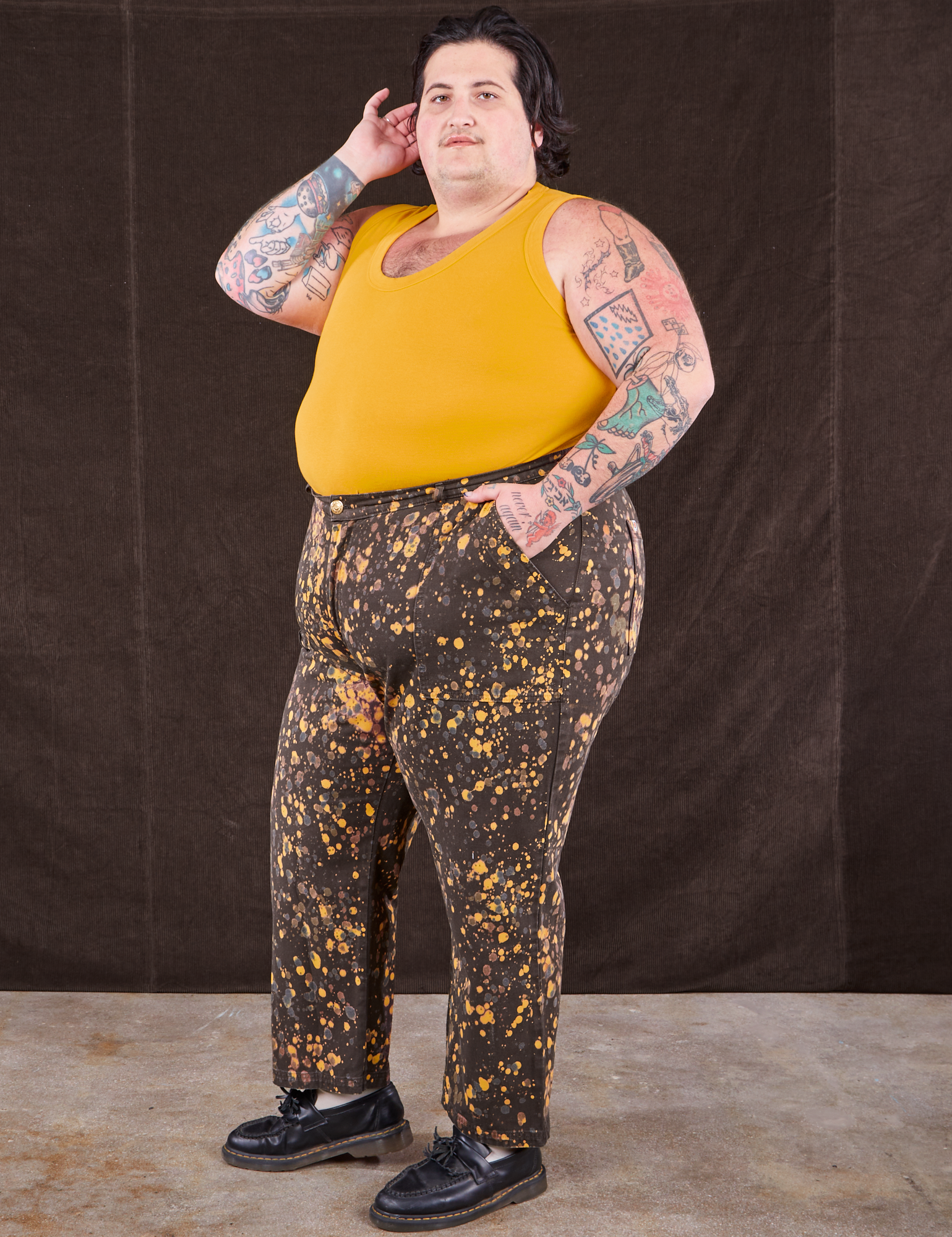 Angled front view of Marble Splatter Work Pants in Espresso Brown and mustard yellow Tank Top on Sam