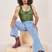Jesse is sitting on a wooden crate wearing Mesh Tank Top in Lawn Green and light wash Sailor Jeans