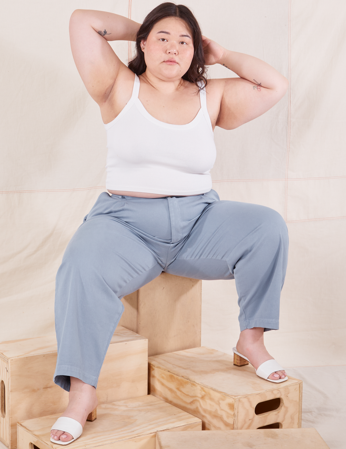 Ashley is sitting on a wooden crate wearing Organic Trousers in Periwinkle and vintage off-white Cami