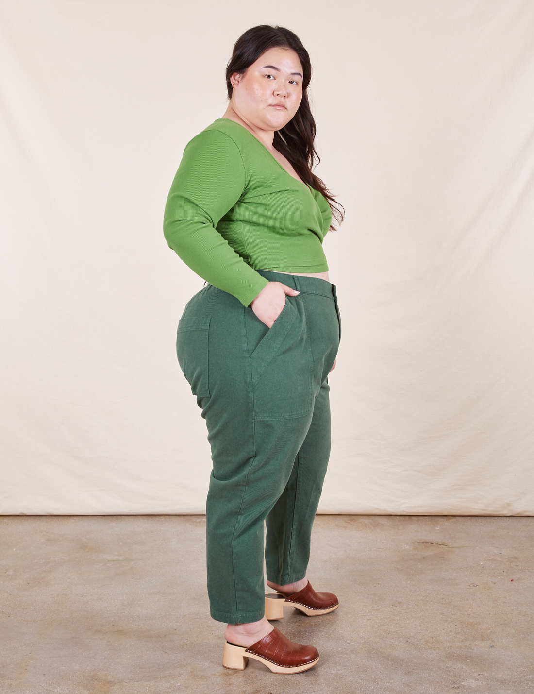 Side view of Pencil Pants in Dark Emerald Green paired with a bright green Wrap Top worn by Ashley