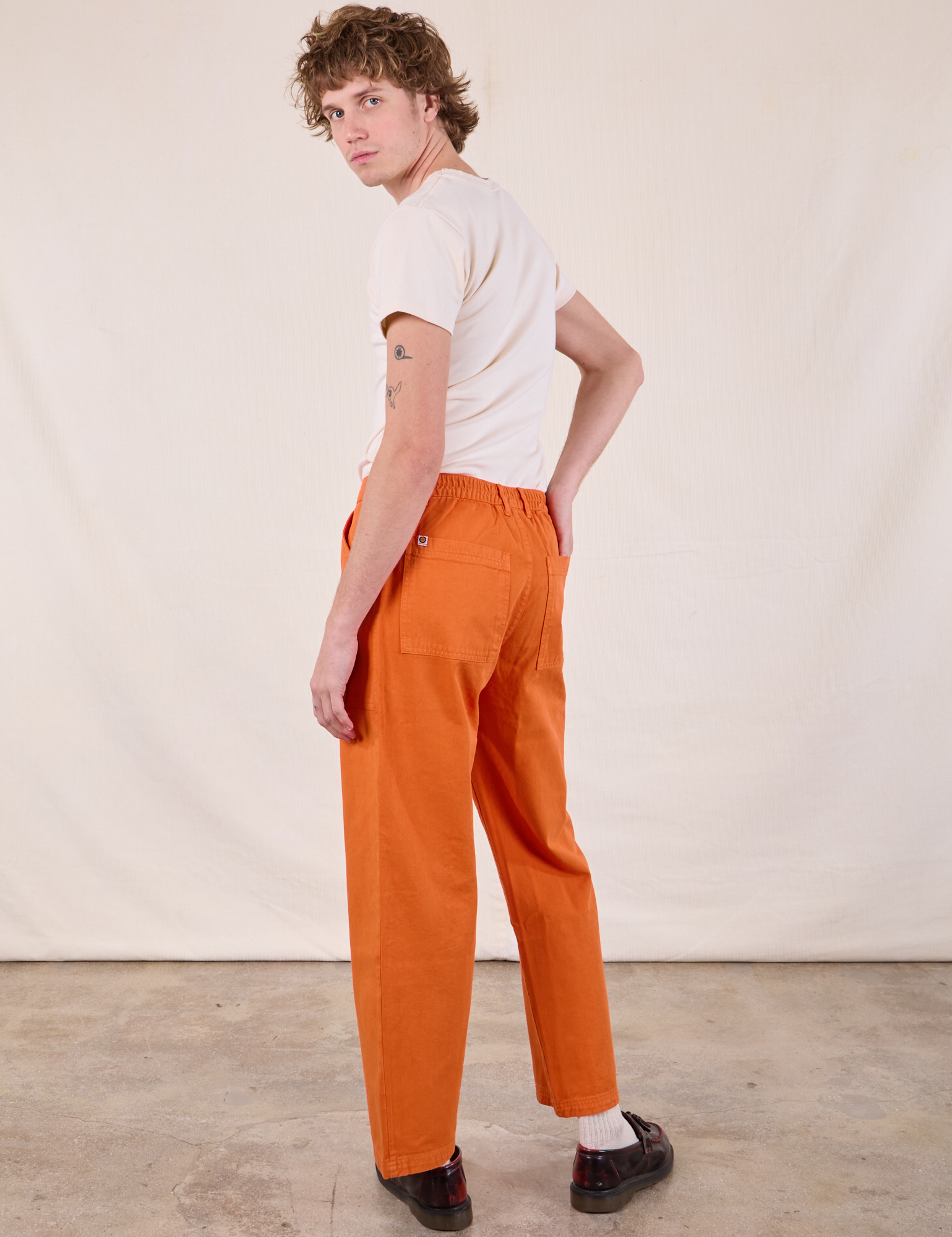 Angled back view of Work Pants in Construction Orange and Burly Tee in Vintage Tee Off-White