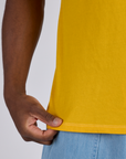 Close up of Isaac holding the bottom hem of Jr. Varsity Tee in Sunshine Yellow