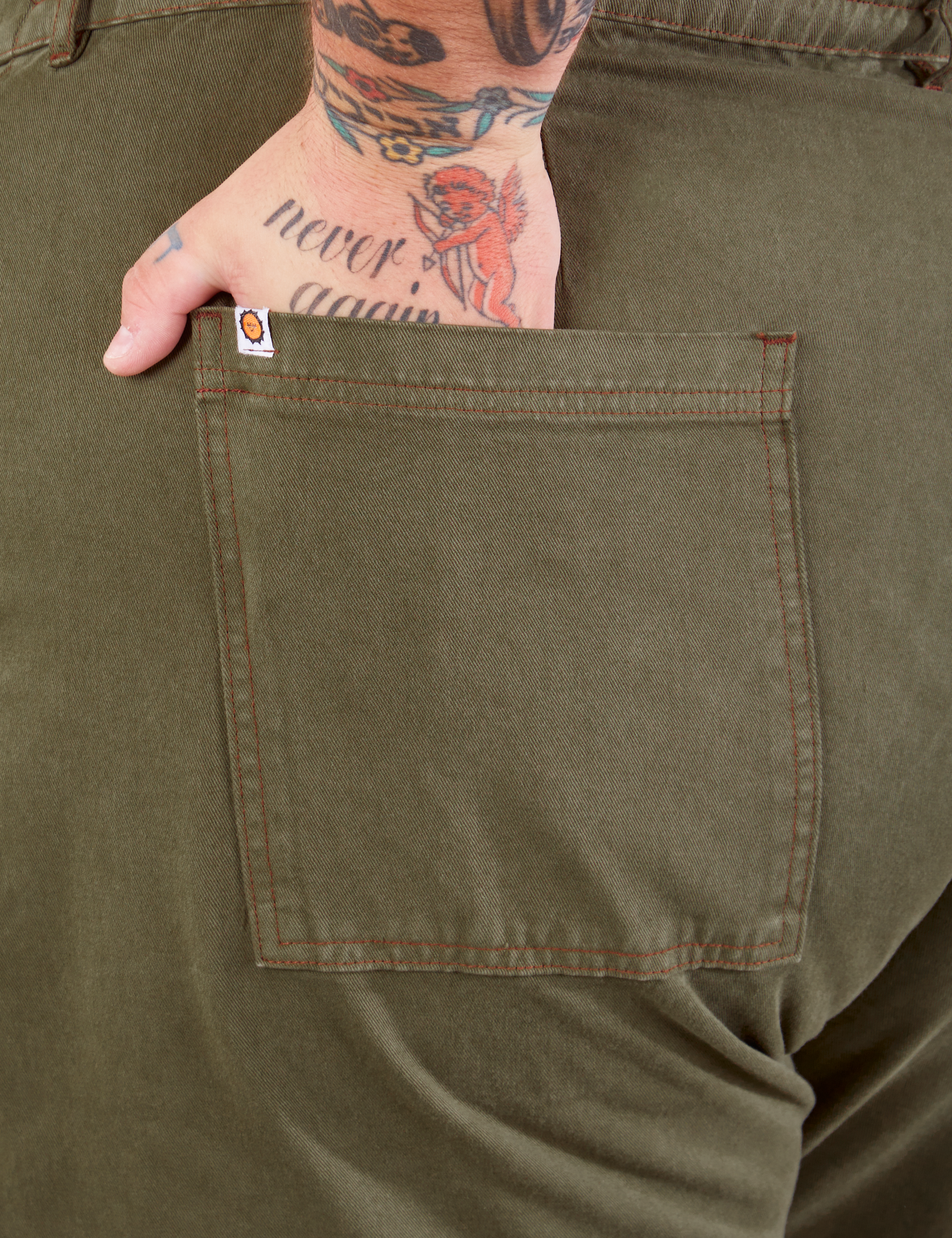 Work Pants in Surplus Green back pocket close up. Sam has their hand in the pocket.