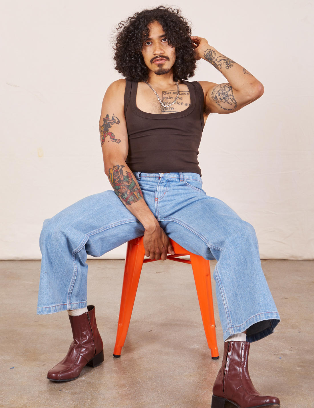 Jesse is wearing Cropped Tank Top in Espresso Brown and light wash Sailor Jeans sitting in an orange stool