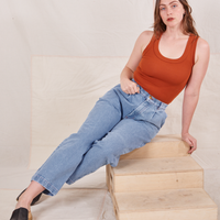 Allison is leaning on a wooden crate wearing Denim Trouser Jeans in Light Wash and burnt orange Tank Top