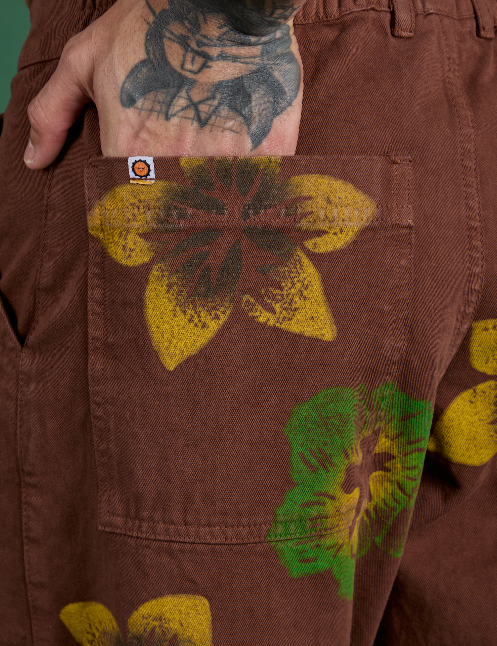 Close up of Jesse's hand in the back pocket of Floral Painted Work Pants in Brown