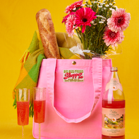 Shopper Tote Bag in Bubblegum Pink with baguette, flowers and scarf inside. Two glasses and a bottle of blood orange soda in front of the bag.