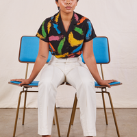 Mika is sitting in between two brass and blue chairs wearing Pantry Button Up in Paint Stroke and vintage off-white Western Pants.