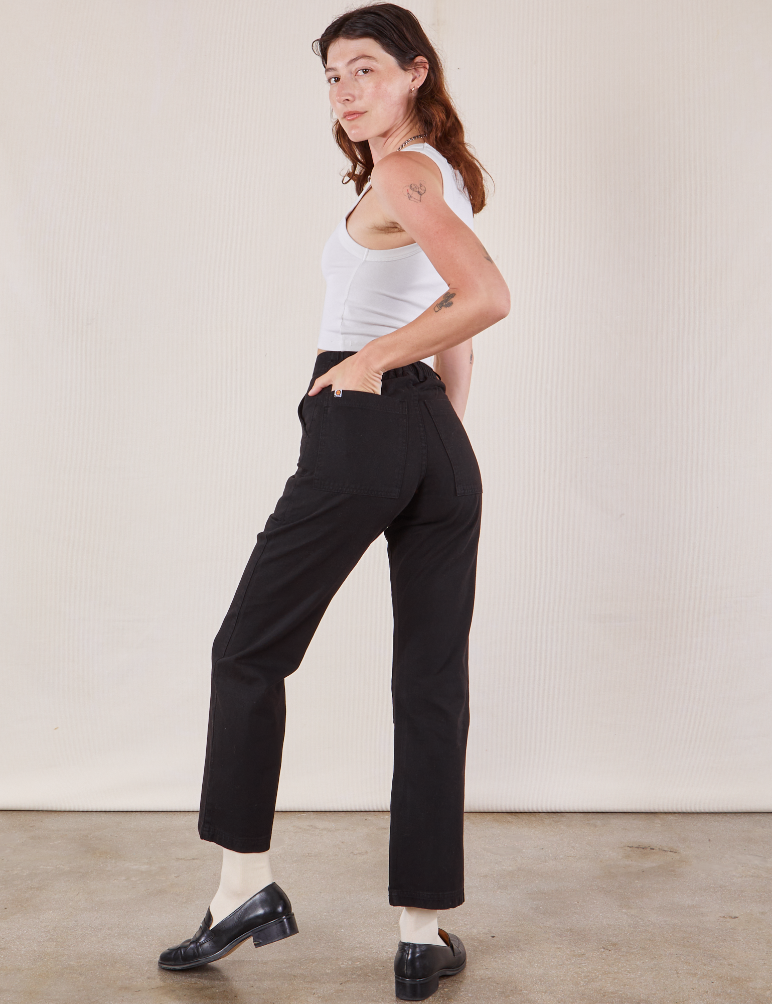 Angled back view of Work Pants in Black and Cropped Tank in vintage tee off-white on Alex