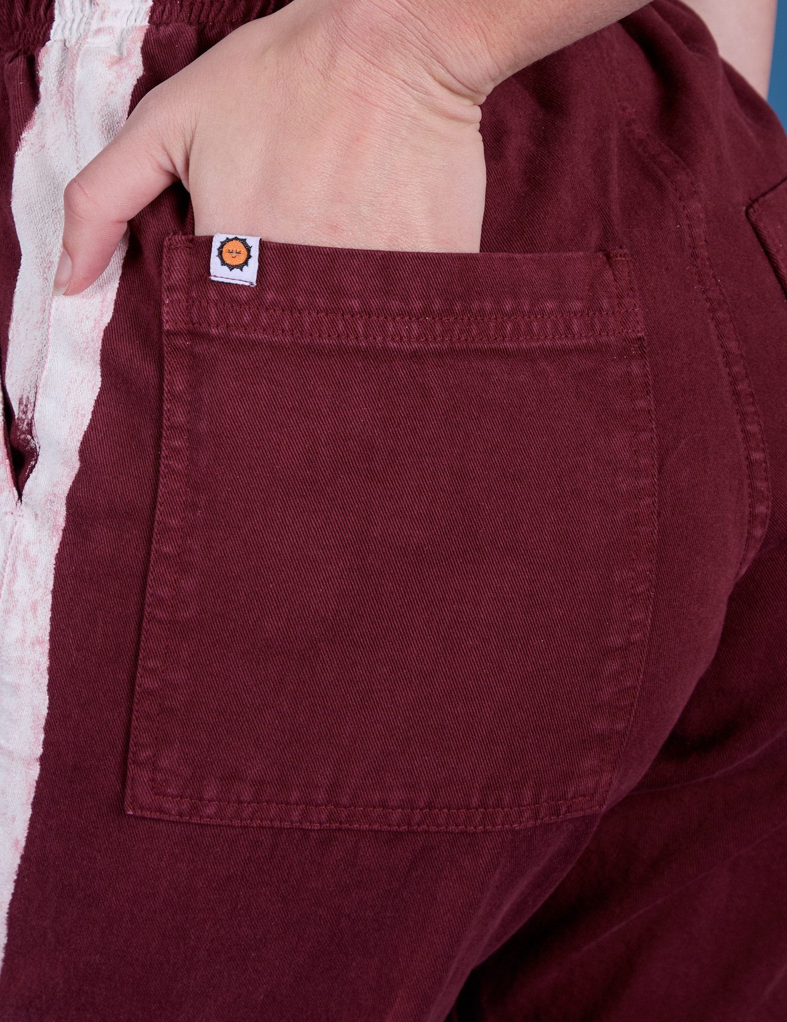 Close up of Alex's hand in the back pocket of Painted Action Pants in Red Wine