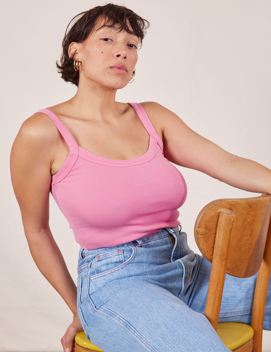 Tiara is sitting in a wooden chair wearing Cropped Cami in Bubblegum Pink and light wash Sailor Jeans