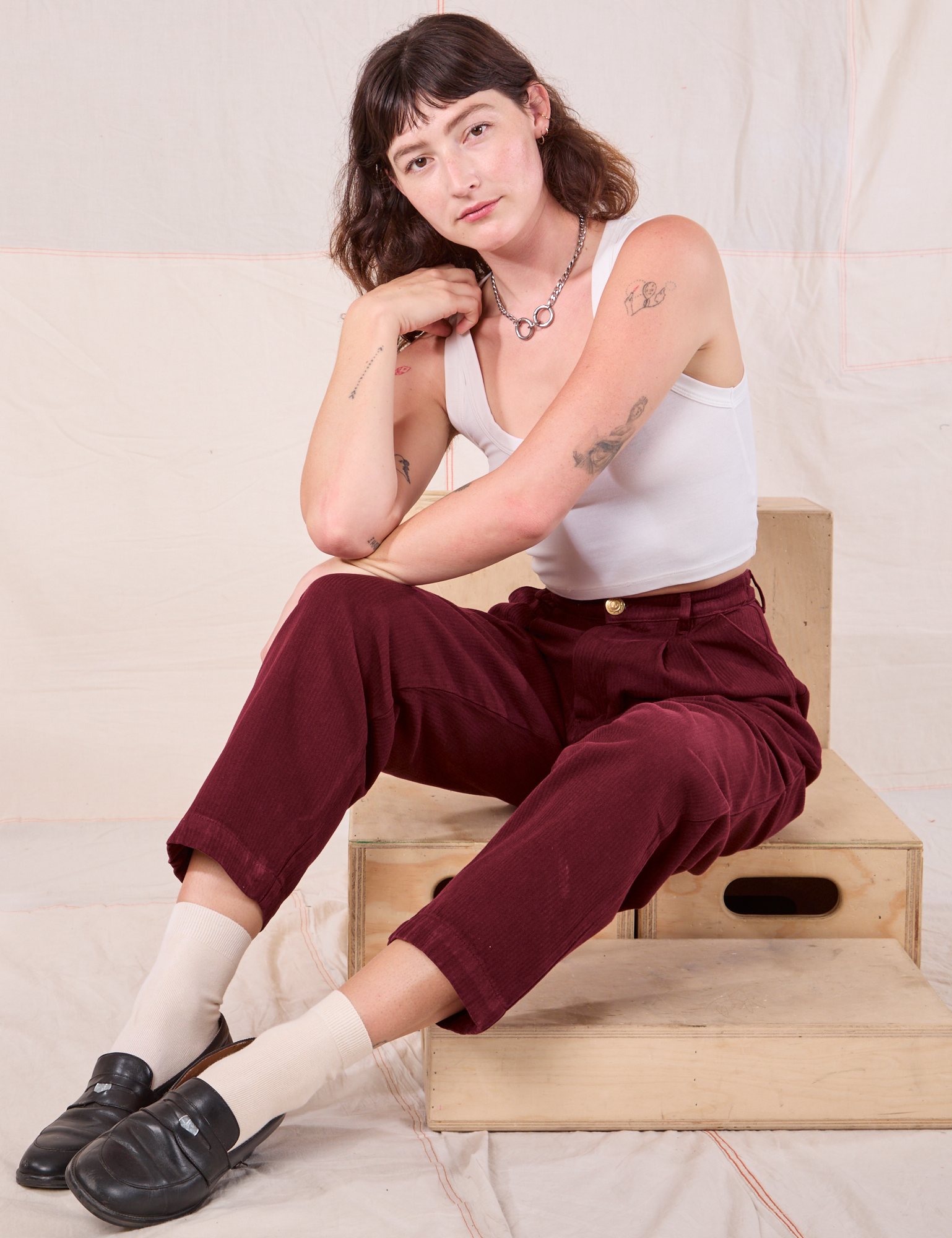 Alex is sitting on a wooden crate. She is wearing Sand Closet 2 Upper Interior and Cropped Tank in vintage tee off-white