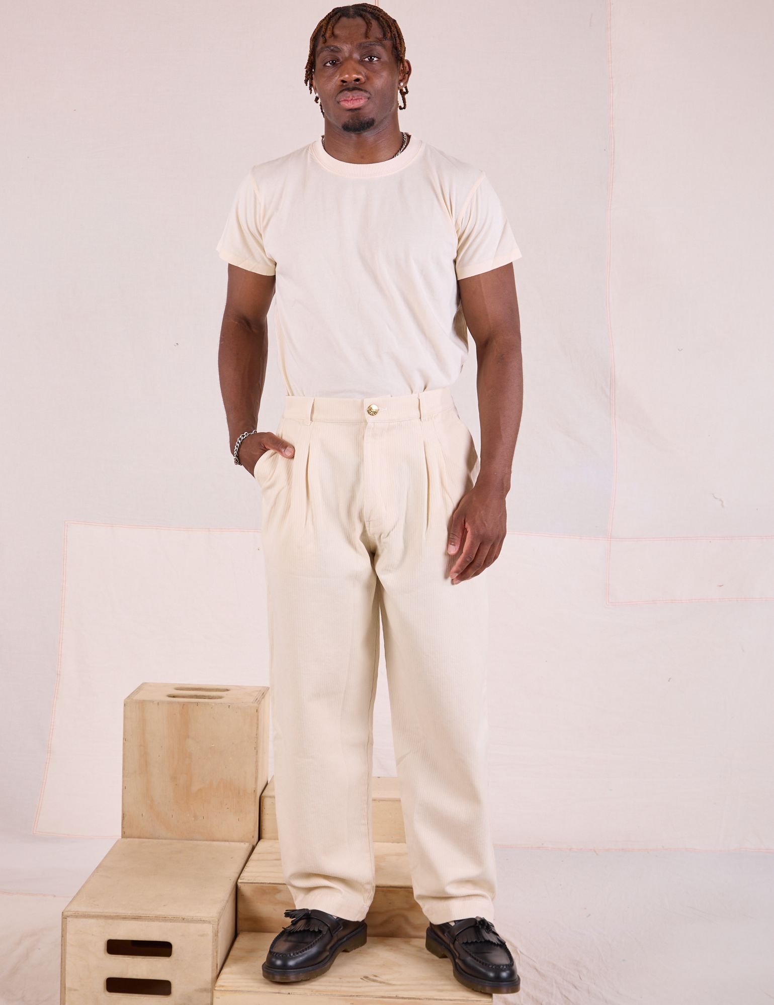 Issac is wearing Heritage Trousers in Natural  and Organic Vintage Tee in vintage tee off-white