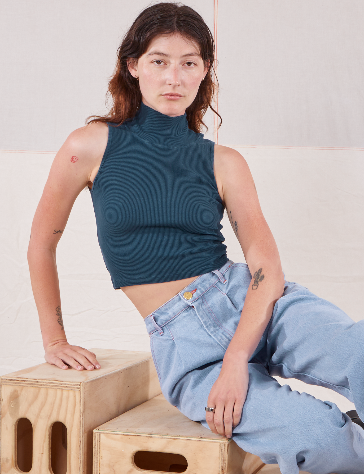 Alex is wearing Sleeveless Essential Turtleneck in Lagoon and light wash Trouser Jeans