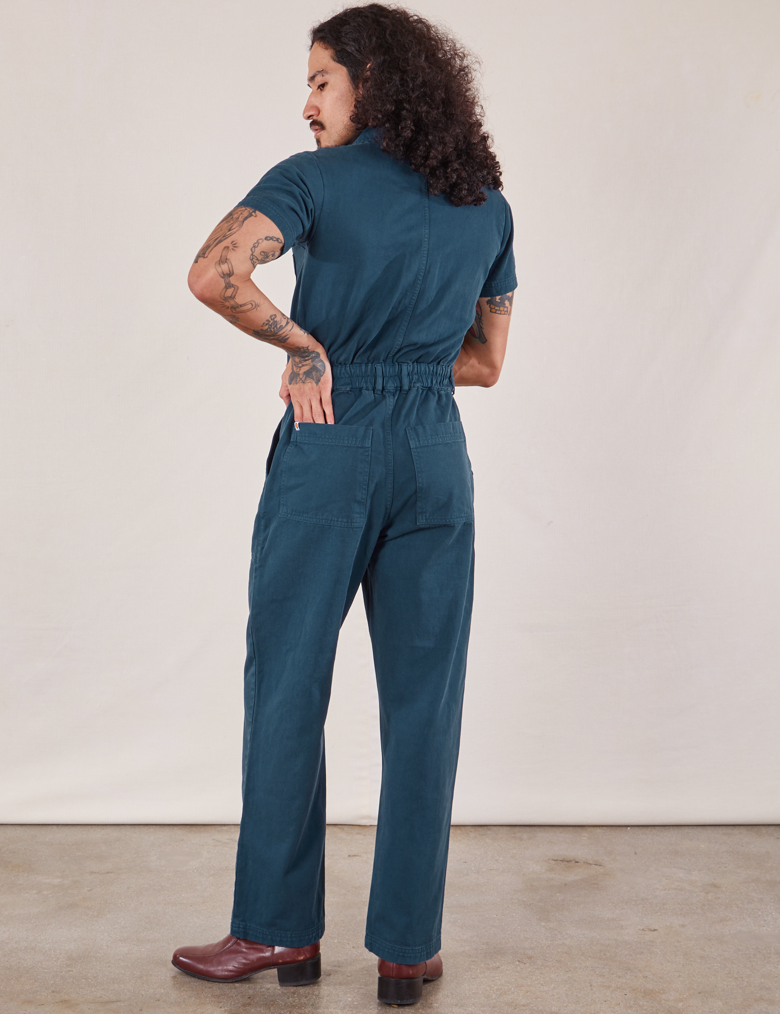 Jesse has their hand on the back pocket of the  Short Sleeve Jumpsuit in Lagoon