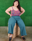 Ashley is wearing Cami in Electric Leopard and marine blue Bell Bottoms. She is sitting on a stack of wooden crates