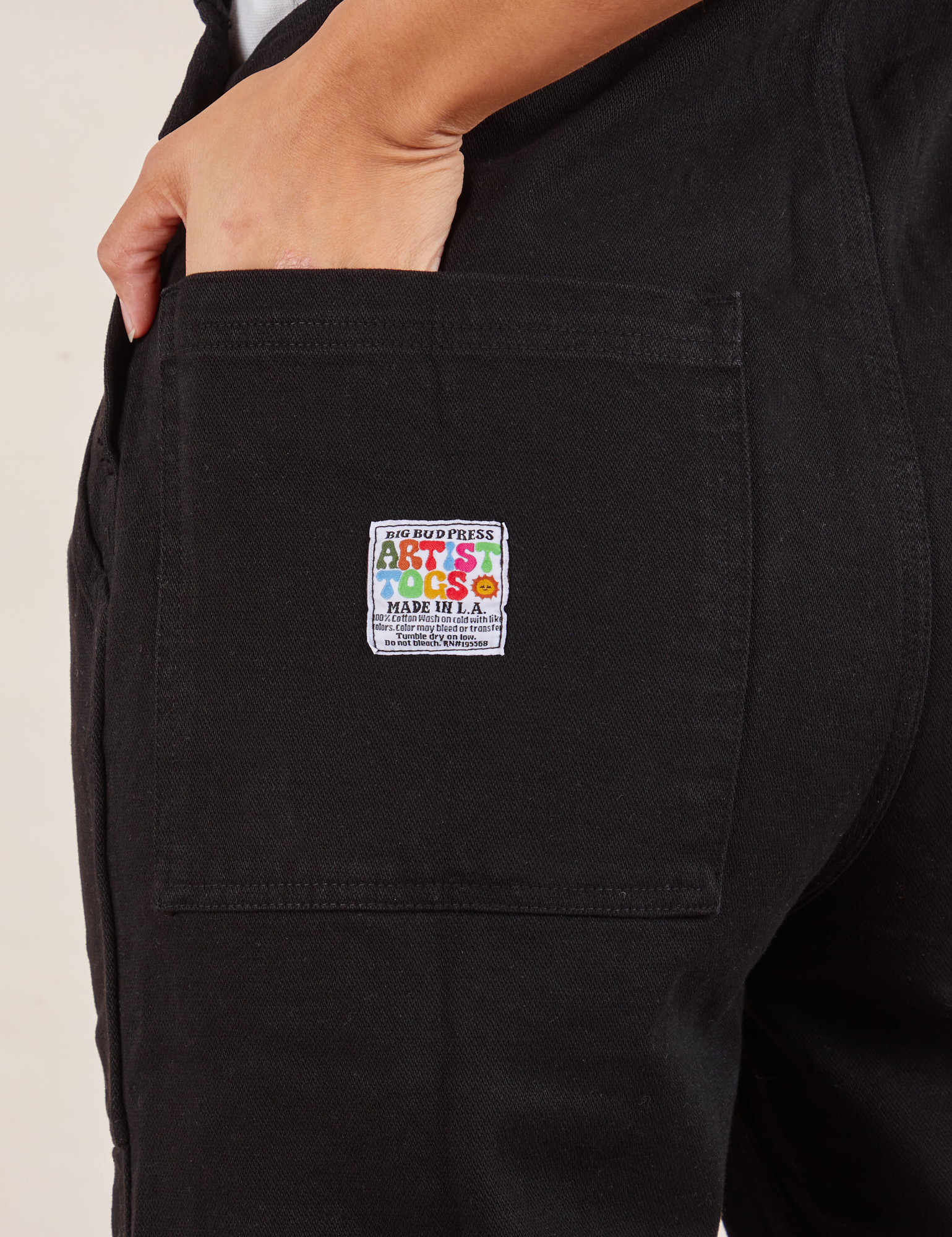 Original Overalls in Mono Black back pocket close up. Tiara has her hand in the pocket.