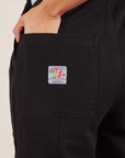 Original Overalls in Mono Black back pocket close up. Tiara has her hand in the pocket.