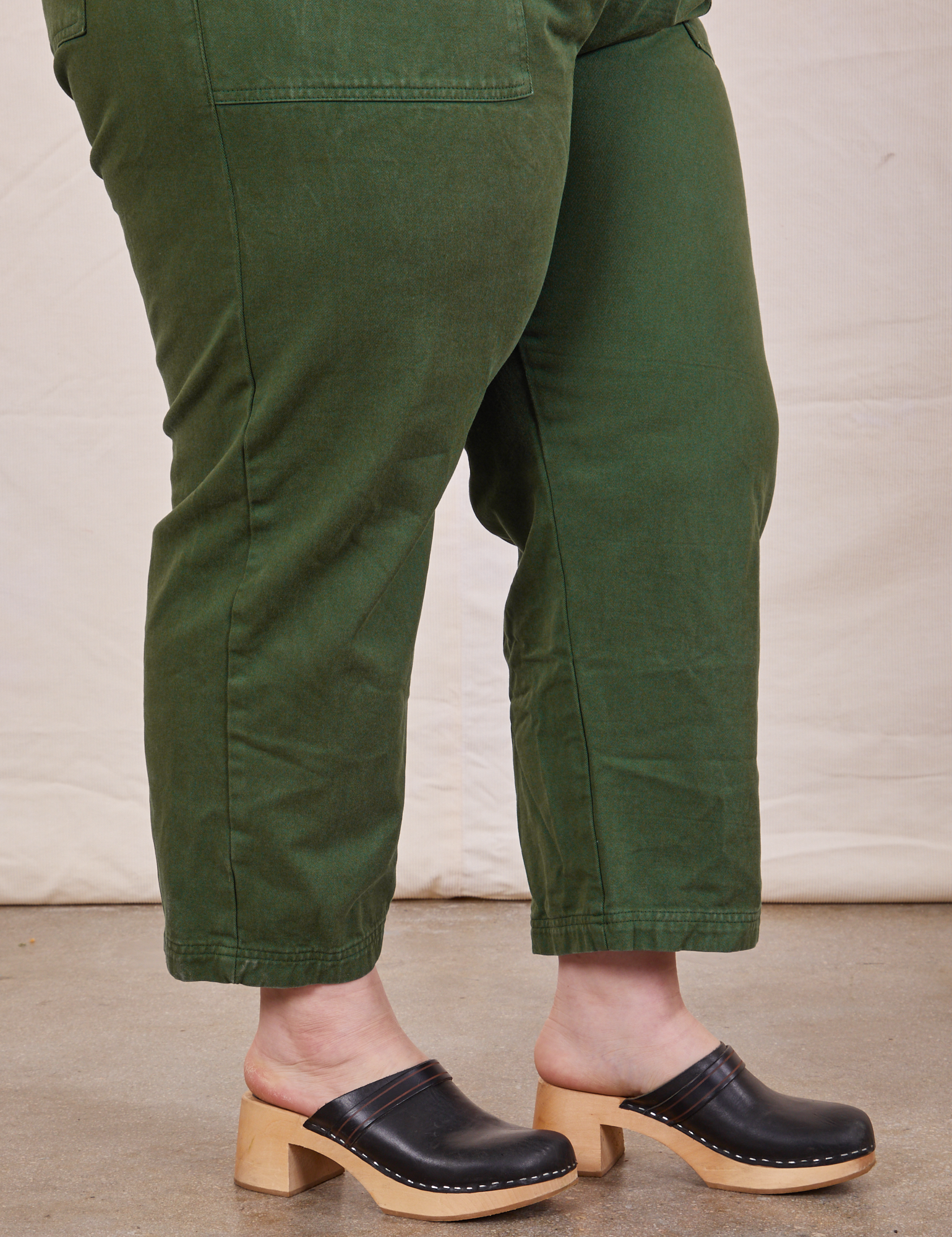 Close up side view of pant leg of Petite Short Sleeve Jumpsuit in Dark Emerald Green worn by Ashley