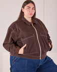 Marielena is wearing a zipped up Mechanic Jacket in Fudgesicle Brown with her hands in the pockets.