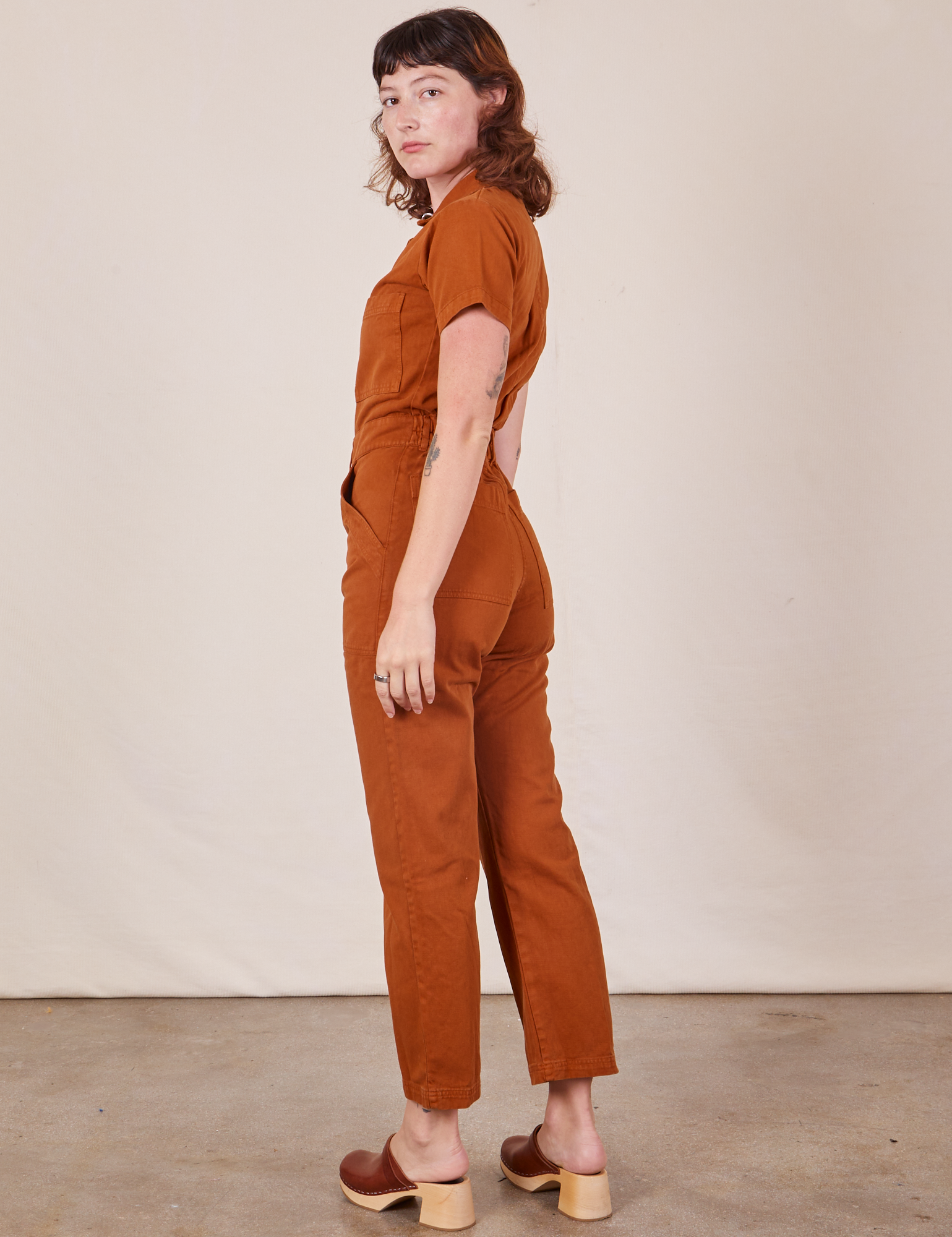 Angled back view of Short Sleeve Jumpsuit in Burnt Terracotta worn by Alex