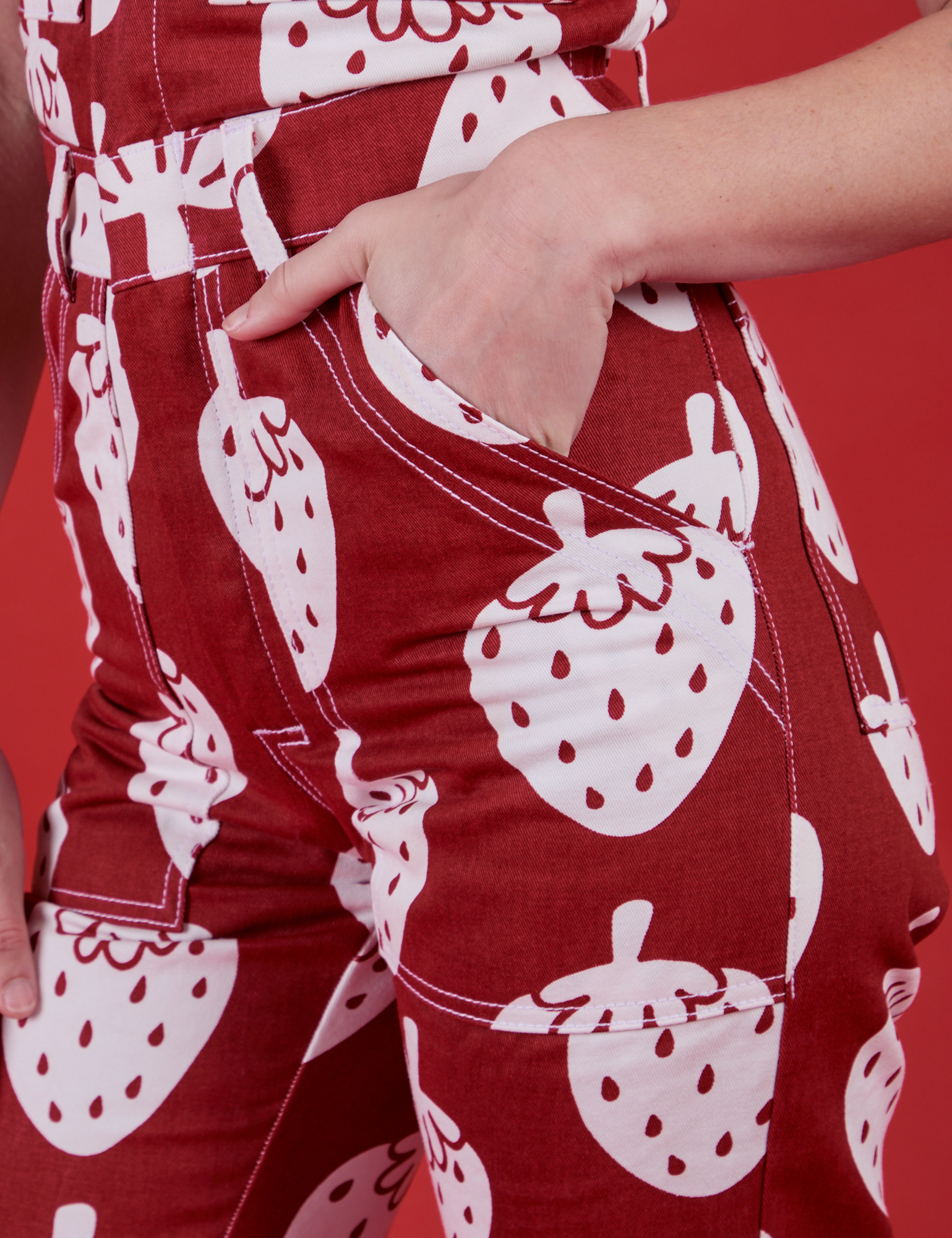 Alex's hand is in the front pocket of Strawbaby Jumpsuit