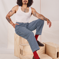 Jesse is sitting on a wooden crate wearing Denim Trouser Jeans in Railroad Stripe and vintage off-white Tank Top