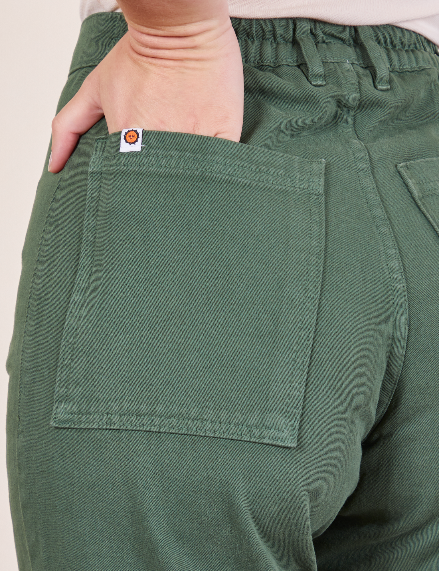 Back pocket close up of Western Pants in Dark Green Emerald. Alex has her hand in the pocket.